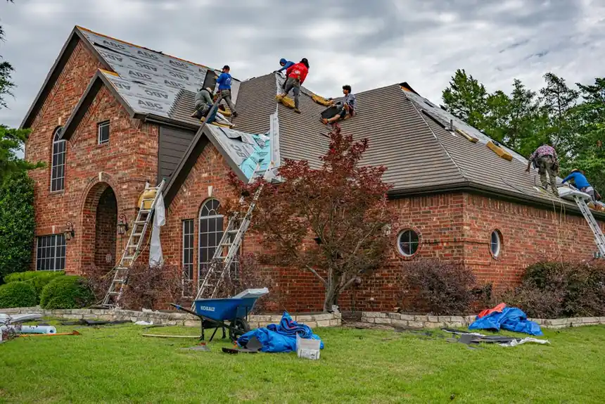 Roofers working on a brick home, installing shingles and roofing materials.